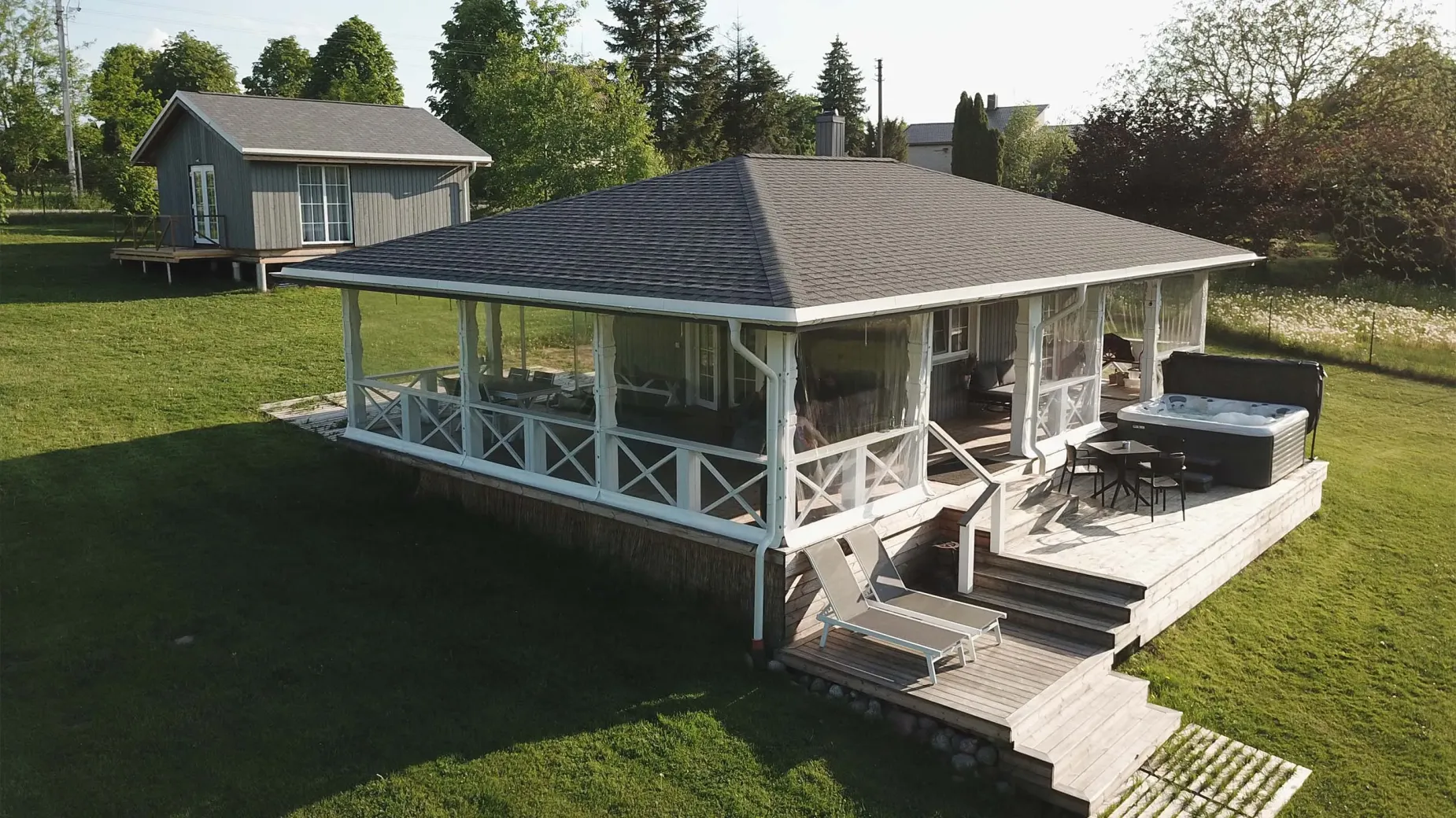 A wooden cottage with a gray roof and a spacious screened porch