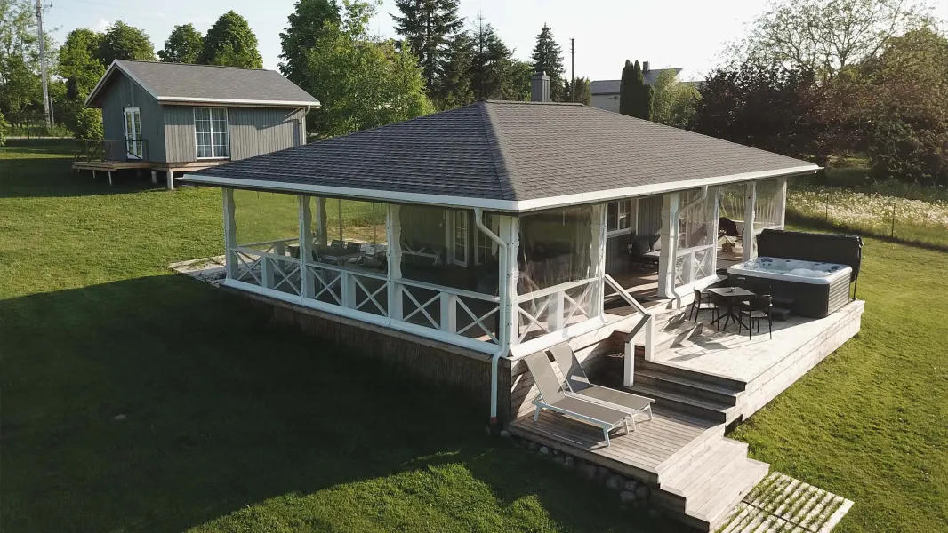 A wooden cottage with a gray roof and a spacious screened porch
